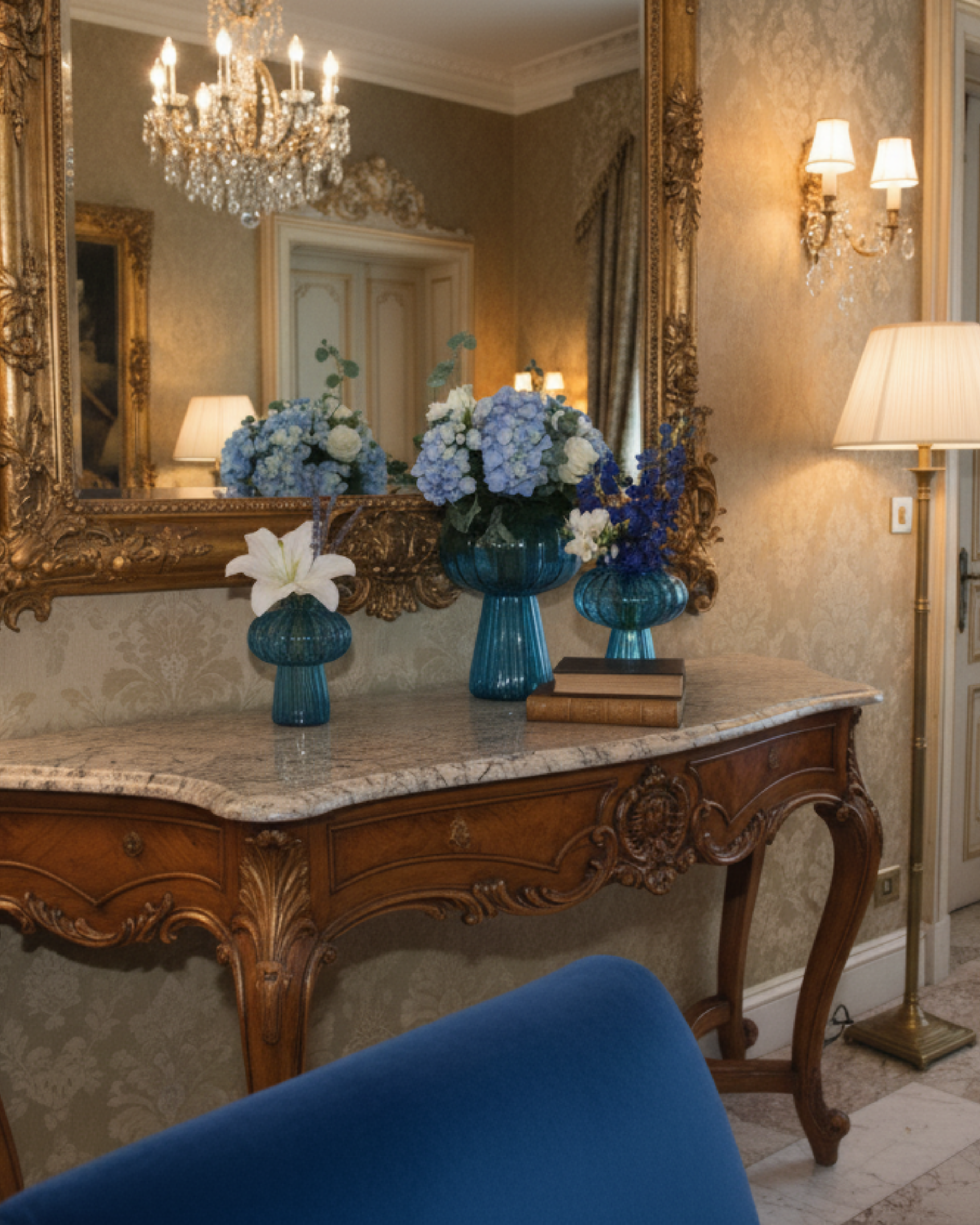 Decorative room with ornate mirror, floral arrangements, and a blue chair.