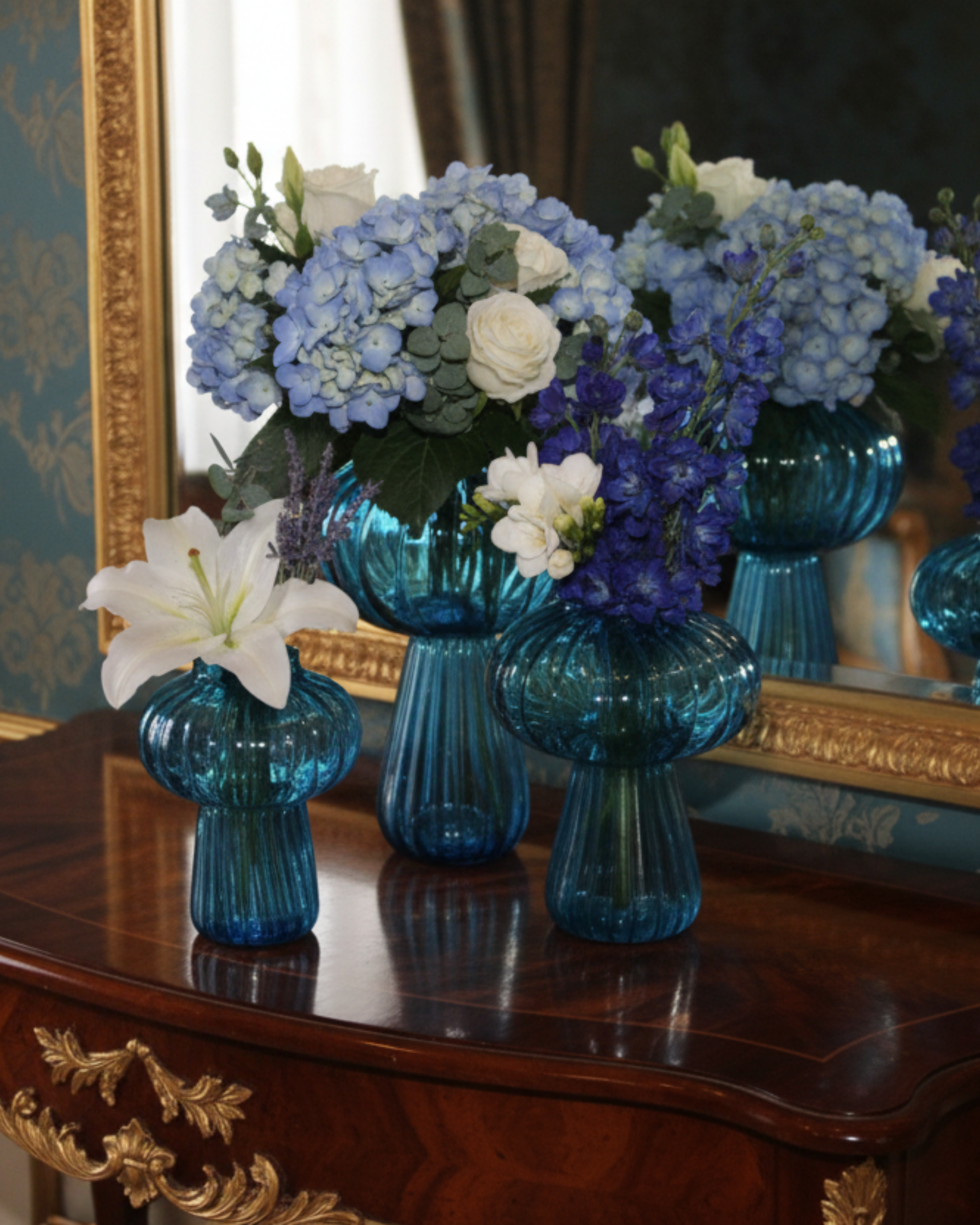 Blue glass vases with floral arrangements on a wooden table with decorative gold frame.