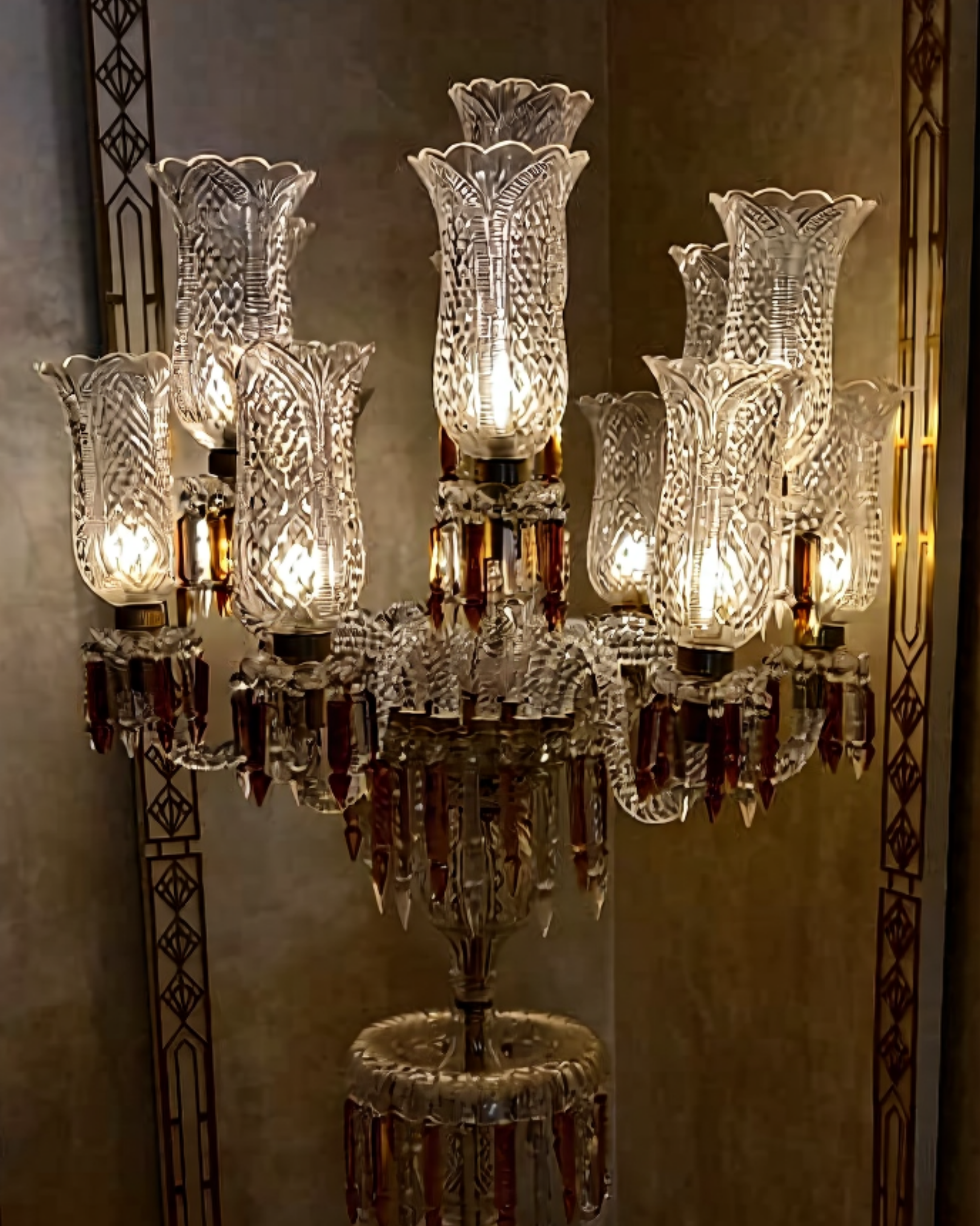 Crystal chandelier with multiple lights against a decorative wall.
