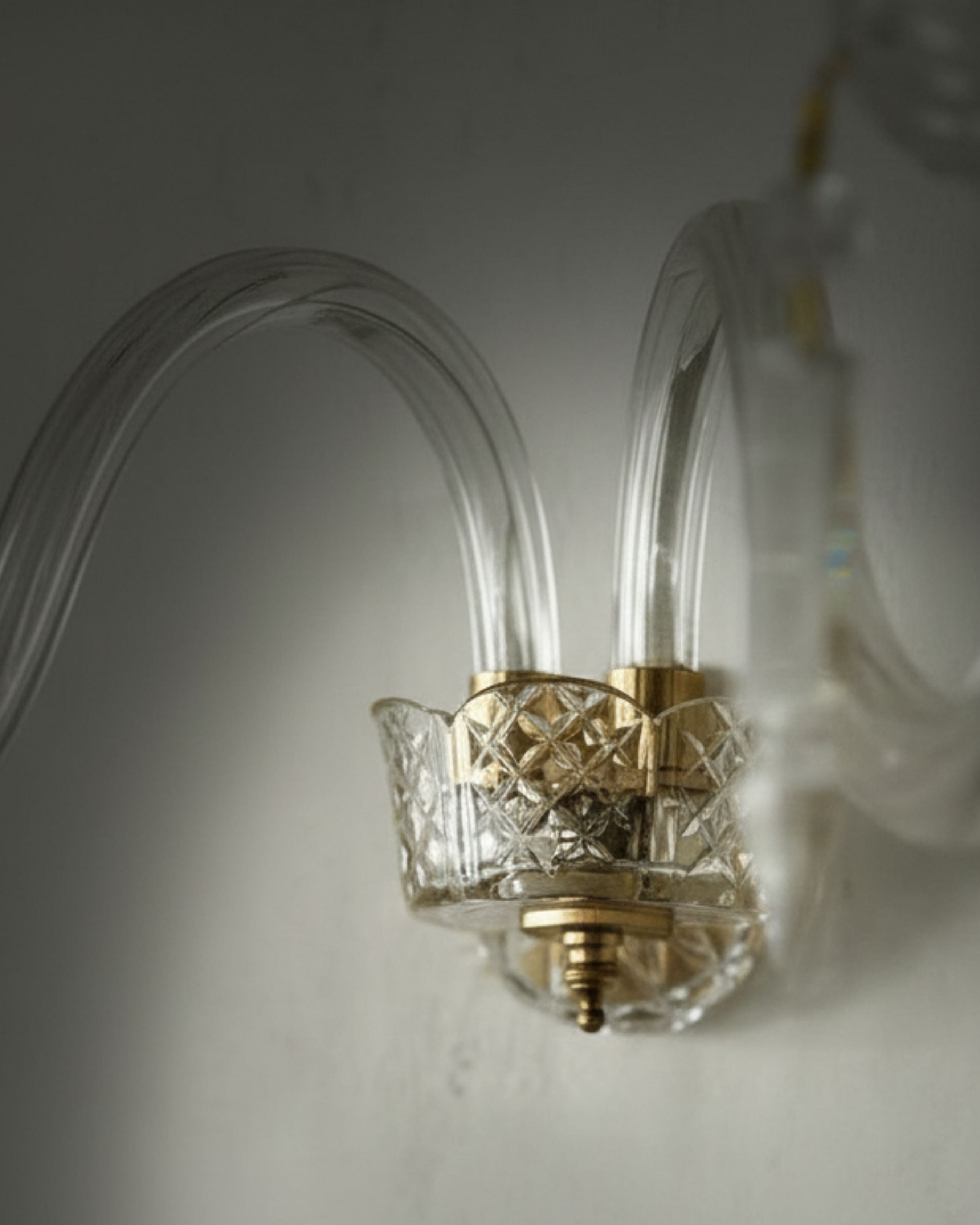Decorative wall sconce with clear glass and gold metal detailing on a neutral background