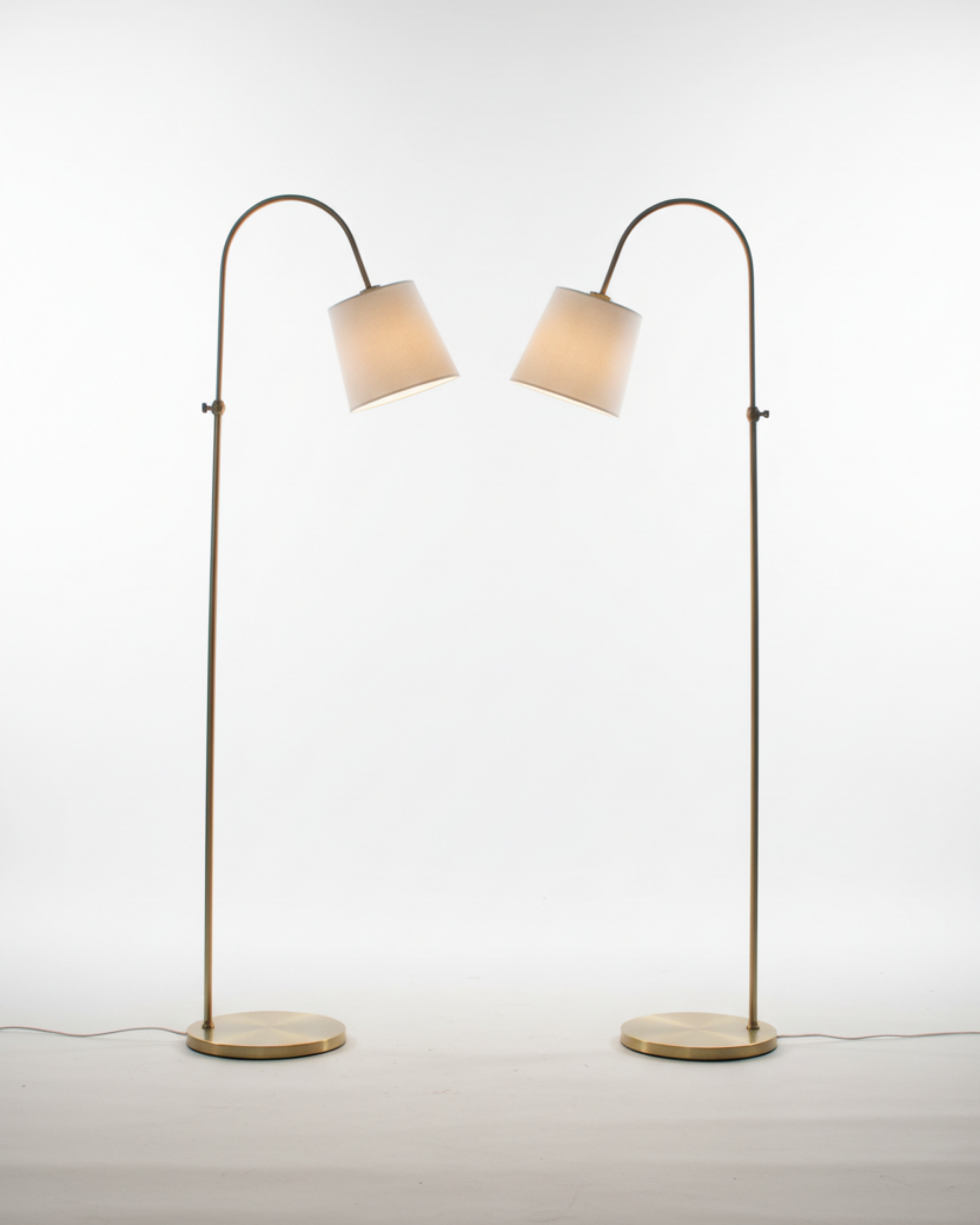 Two floor lamps with curved arms and white lampshades on a light gray background