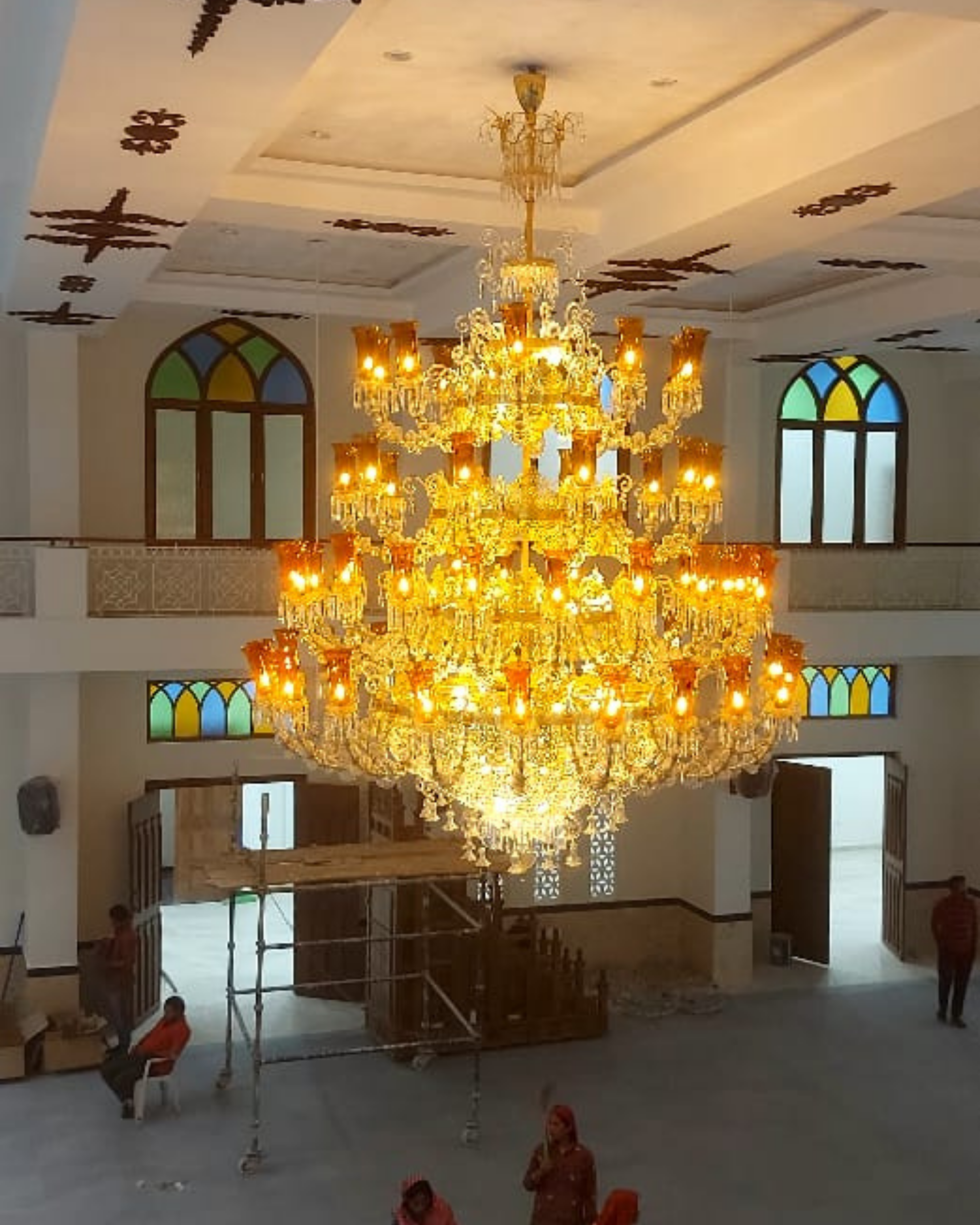 Large chandelier in a room with stained glass windows and people in the background