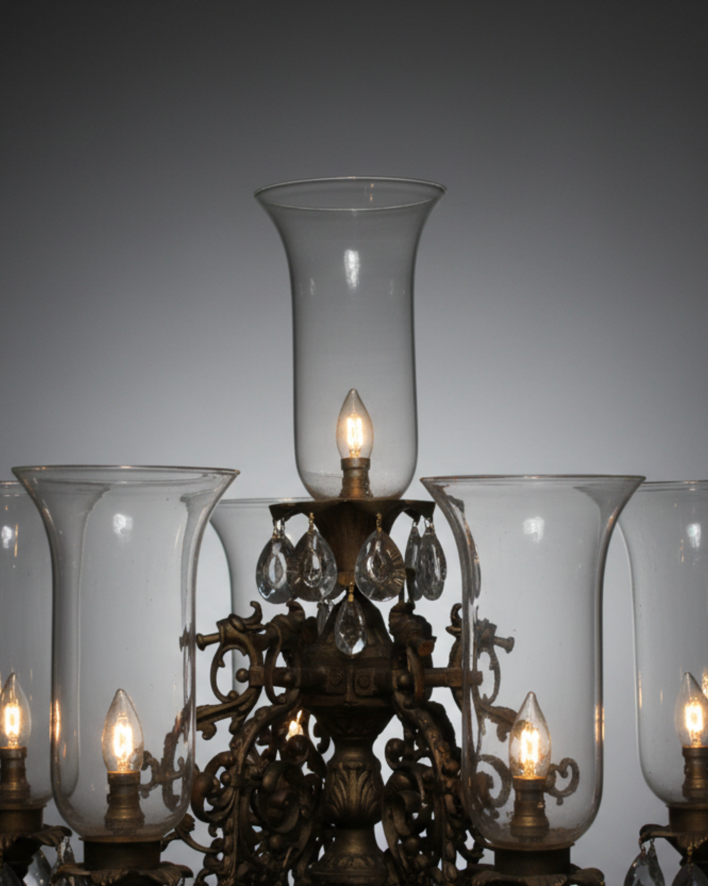 Decorative chandelier with clear glass shades and lit bulbs against a gray background