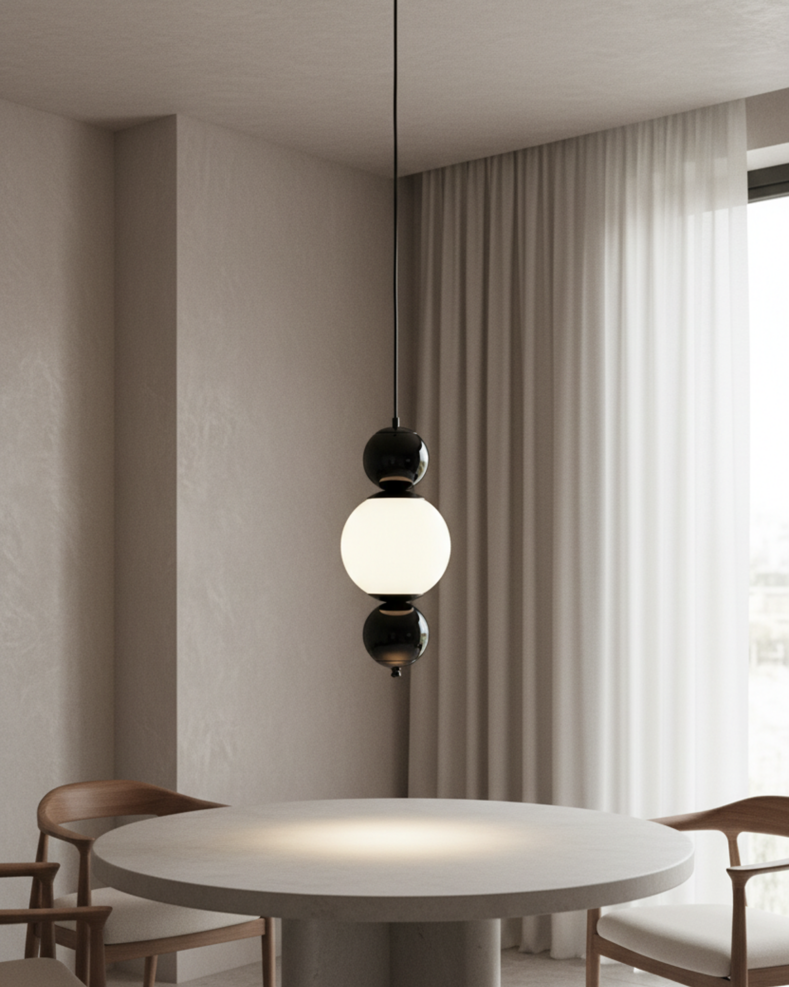 Modern pendant light hanging above a round table in a room with neutral walls and curtains the Noor Orb Pendant Light is a statement of understated luxury. The design features a luminous handcrafted glass sphere, framed gracefully by solid brass accents that add warmth, contrast, and durability.