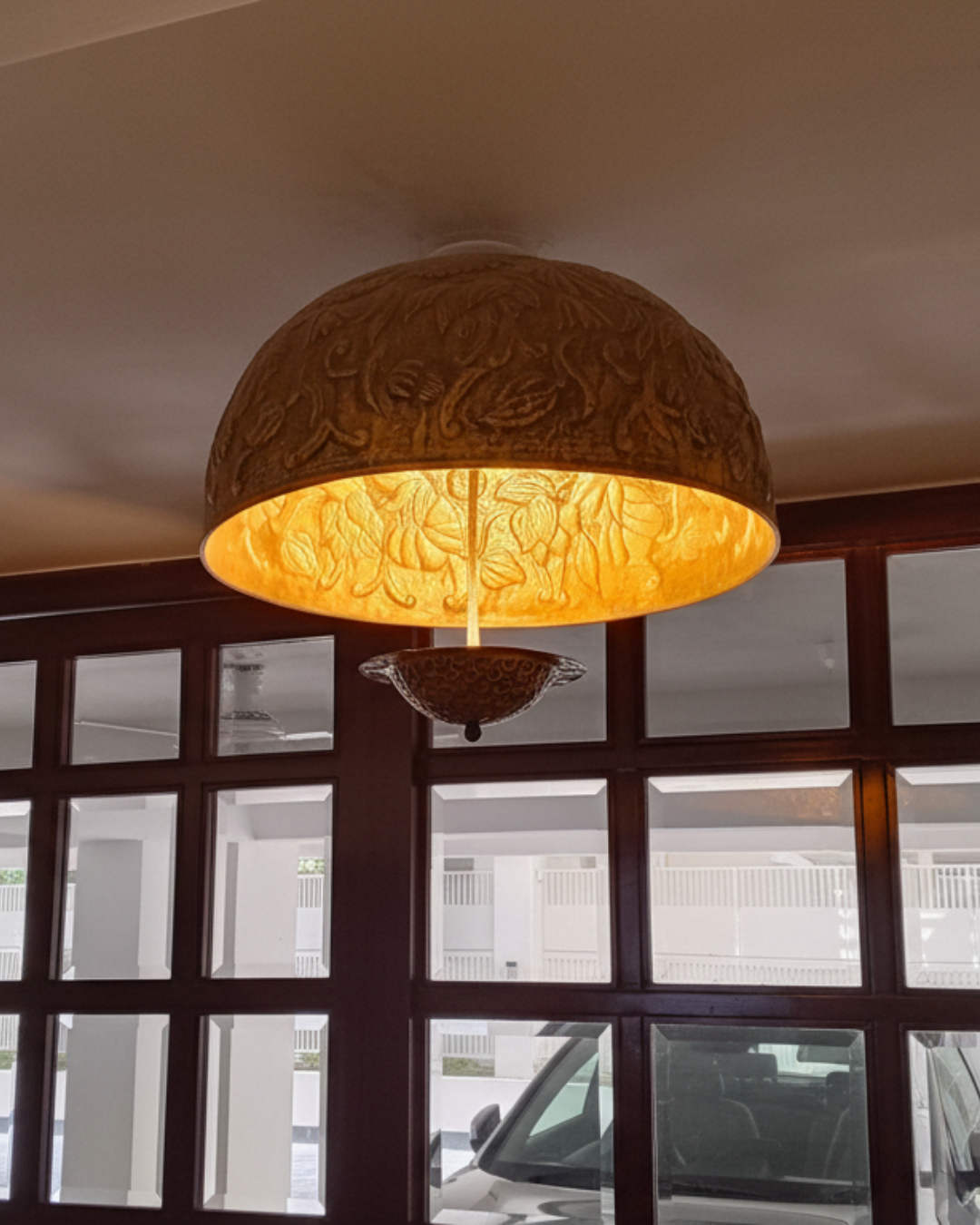 Decorative ceiling light fixture with intricate design in a room with glass windows.