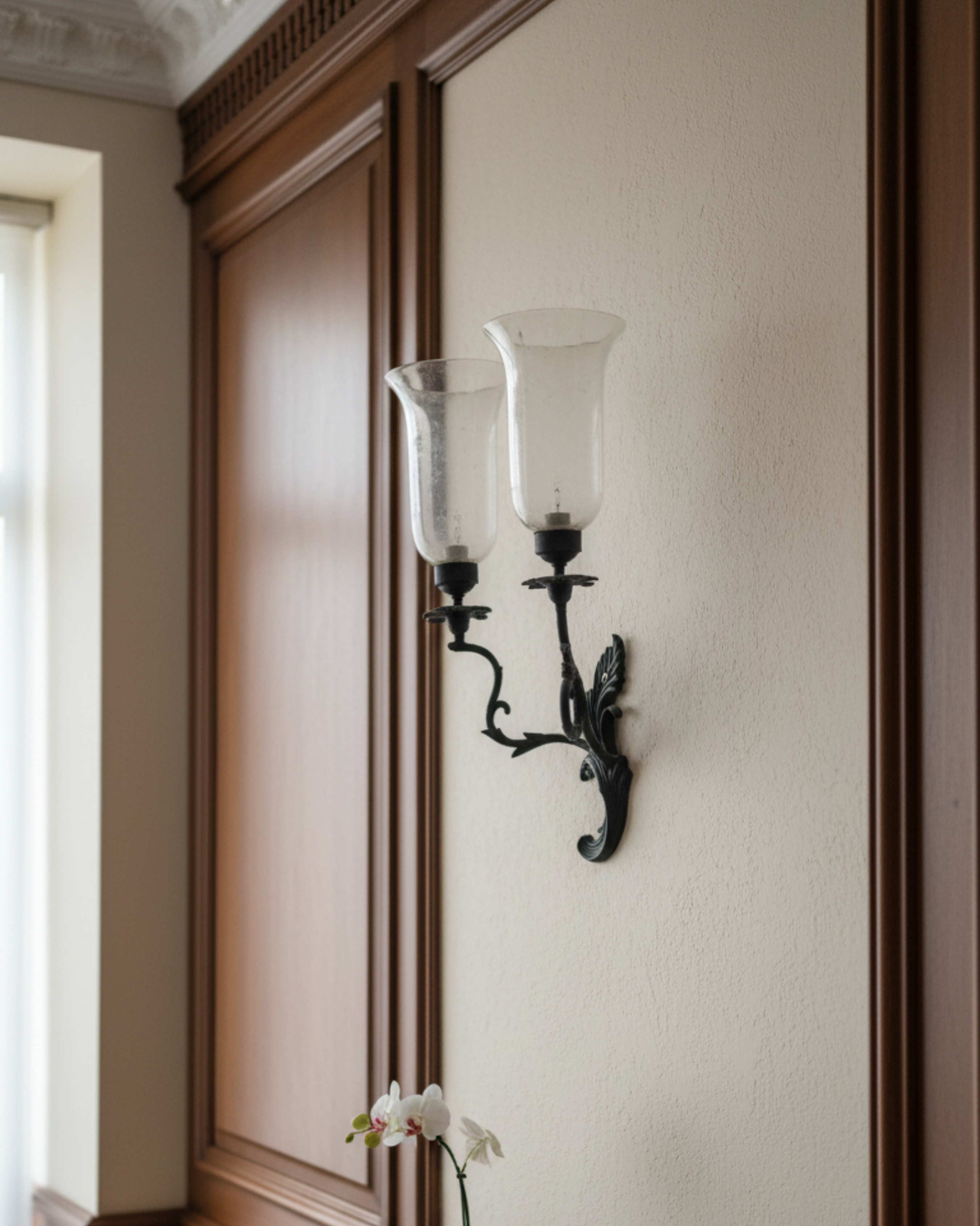 Decorative wall sconce with glass shade on a wall with wooden paneling.