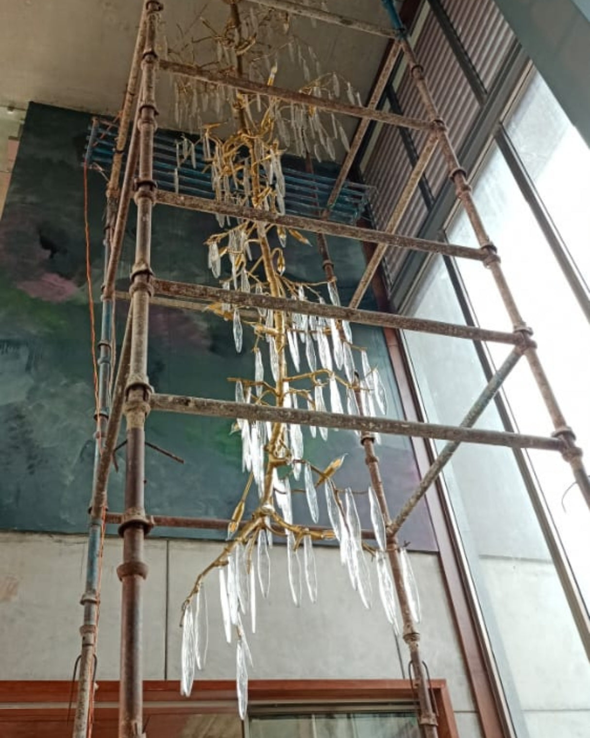 Vriksha Jyoti inspired by weeping willow Decorative chandelier hanging from a ceiling with scaffolding below